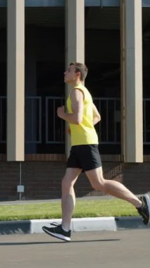 Dikey Ekran: Ağır çekim formalı ve şortlu bir adam modern binaya karşı sütunlarla koşuyor. Güneşli bir sabahta şehirde atış talimi. Sağlıklı yaşam tarzı kavramı