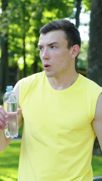 垂直屏风 在公园慢跑后身穿黄色瓶盖饮用水的肌肉男 在炎热的夏日早晨锻炼身体后 手持运动员感到很疲倦 健康的概念 — 图库视频影像