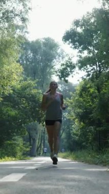 Yavaş çekim sportif kadın yeşil ağaçların arasında asfalt yolda koşuyor. Sabah güneşinde kadın atlet antrenmanı. Zindelik kavramı