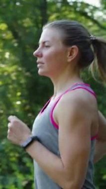 Spor bluzu giyen, spor bileklik takan, parkta koşan, ağaçların arasından parlayan yavaş çekim zinde bir kadın. Atış talimi dışarıda yapılıyor. Zindelik kavramı