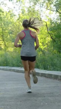 Dikey ekran: Atkuyruklu sarışın kadının spor şort giydiği ve yuvarlak yolda üst üste koşu yaptığı bir fotoğraf. Güneşli bir sabahta dışarıda antrenman yapan bayan sporcu. Zindelik kavramı