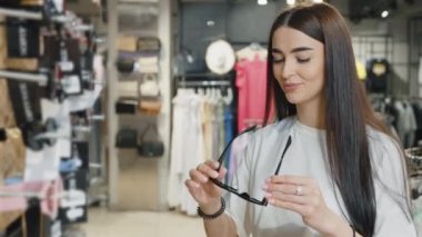 Genç bir kadın süpermarkette güneş gözlüğü deniyor. Bayan müşteri tatil için aksesuar alıyor, kameraya bakıyor ve gülümsüyor. Alışveriş kavramı