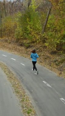 Dik ekran: Sonbahar parkında kadın koşucu spor giyiniyor, yavaş çekimde, yukarıdan çekiliyor. Aktif bir insanın sabahları egzersiz yaptığı arka plan görüntüsü. Sağlıklı yaşam tarzı kavramı