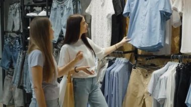 Neşeli arkadaşlar giysi dükkanında birlikte alışveriş yapıyorlar. Genç kadınlar erkek giyim bölümünden bir gömlek seçiyorlar. Moda kavramı