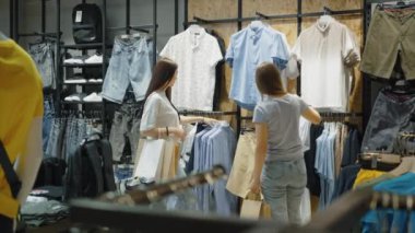Two young women are choosing a shirt in the mens clothing department. Female costumers shopping and spending time together