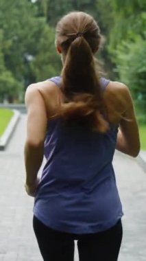 At kuyruklu, spor giysili, parkta ağır çekimde koşan genç bir kadın. Atış yapan atletik kadın dışarıda kardiyo antrenmanı yapıyor. Zindelik kavramı