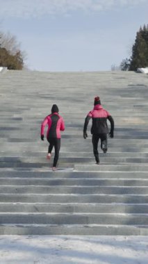 Spor kıyafetleri giyen insanlar geniş beton merdivenlerde koşuyor, arka planda mavi gökyüzü. Güneşli bir kış gününde arka manzara koşucuları birlikte egzersiz yapıyor. Sağlıklı yaşam tarzı kavramı