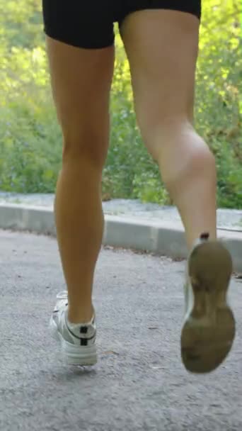 垂直スクリーン 夏のアスファルトロードで走るショートパンツを着用する女性のスローモーション脚 外部の女性アスリートのトレーニングのショット部分的なビューを追跡 フィットネスの概念 — ストック動画