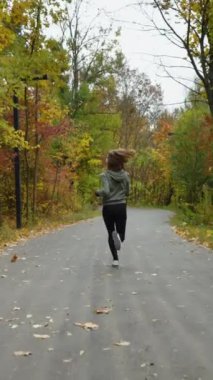 Yavaş çekimde koşan kadın koşucu turuncu ve sarı ağaçların yanından geçiyor. Aktif bir kadının sonbahar sabahı dışarıda egzersiz yaparken çekilen görüntüsü. Sağlıklı yaşam tarzı kavramı