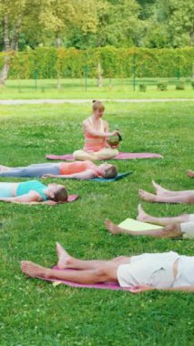Dikey Ekran: Yogi kadın meditasyon sırasında sopayla şarkı söylerken pratisyenler çimlerin üzerinde ceset pozisyonunda yatıyorlar. yoga sınıfı derin restorasyon, beden ve zihin rahatlatma konsepti