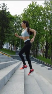 Yeşil parktaki merdivenlerde koşan atkuyruklu, spor tişörtlü ve taytlı sağlıklı bir kadın. Şehirde egzersiz yapan kadın koşucunun izini sürüyorum. Zindelik kavramı