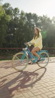 Şehir caddesinde bisiklet süren ve güneşli bir günde gülümseyen güzel, neşeli bir kadın. Bisikletli genç bir kadın mutlu ve rahat, hafta sonu tatili