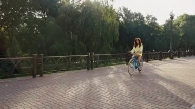 Şehir caddesinde bisiklet süren ve güneşli bir günde gülümseyen güzel bir kadın. Bisikletli genç bir kadın mutlu ve rahat, hafta sonu tatili