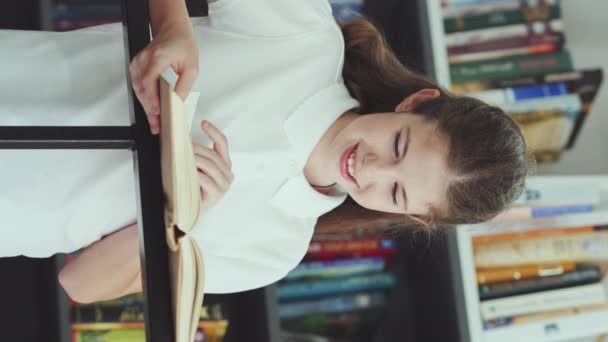 垂直屏风 快乐的女孩穿着马球衫 站在书架上看书 儿童在书店或学校图书馆欣赏文学的肖像 教育的概念 — 图库视频影像