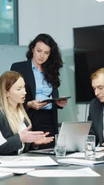 Dikey ekran: İş adamları ofiste toplanıyor, toplantı yapıyor, projeleri tartışıyor, kağıtlarla, laptopla çalışıyor, tablet kullanan bir kadın. Planlama stratejisi, yöneticilerin iletişimi