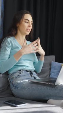 Dikey Ekran: Gündelik giyinen neşeli kadın rahat bir şekilde kanepede oturuyor ve bilgisayarla video görüşmesi yapıyor. Salgın sırasında evde çalışan bir iş kadınının izini sürüyorum. Müşteriyle çevrimiçi toplantı