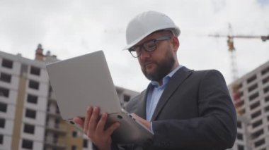 Sakallı, koruyucu başlıklı inşaat mühendisi inşaat alanında yapılan işler hakkında not defterine önemli notlar alıyor. Düşük açılı adam inşaat alanını inceliyor. Kontrol kavramı
