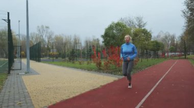 Güz parkındaki spor salonunda spor giyim bölümünde koşan yetişkin bir kadın. Atış talimi yapan sporcu dışarıda. Fitness ve sağlıklı yaşam tarzı