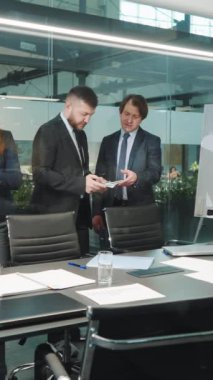Dikey ekran: Resmi olarak işadamları ofiste masanın başında oturmuş projeyi tartışıyor, bilgi aramak için akıllı telefonları kullanıyorlar. Konferanstaki şirket yöneticileri. İş kavramı