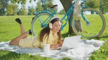 Hasır şapkalı ve kulaklıklı genç bir kadın yeşil çayırda dizüstü bilgisayar izliyor. Ağaçların yanında mavi bir bisiklet. Dudaklarında gülücüklerle yukarı bakan romantik bir kadın. Yalnızlık ve ilham arayışı