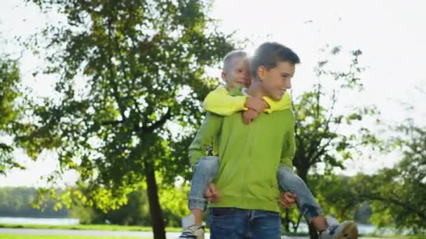 Šťastný Chlapec Otáčí Bratrem Ramenou Slunečném Parku Usmívající Puberťačka Která — Stock video