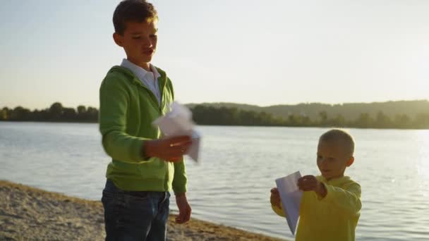 Dva Šťastní Bratři Hrají Papírovými Letadly Písečném Břehu Řeky Kluci — Stock video