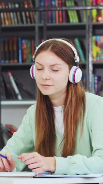 Vertical Screen Caucasian Schoolgirl Wearing Headphones Daydreaming While Sitting Table — Stock Video