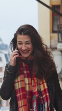 Dikey Ekran: Uzun saçlı, deri ceketli ve kaşkollü neşeli bir kadın şehirde yürürken ve telefonda konuşurken kahkahalara boğuluyor. Taşınabilir bağımlılık kavramı