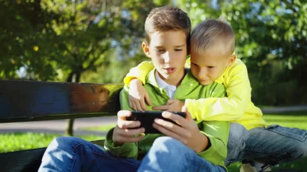 Starszy Brat Pokazuje Coś Młodszemu Smartfonie Parku Dzieci Spędzają Cały — Wideo stockowe