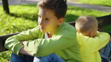 Tartışmadan sonra parkta sırt sırta oturan iki kardeş. Erkekler birbirlerine kızgındır. Kardeşler sürekli kavga eder, kimse pes etmek istemez..