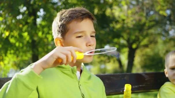 Preteen Chlapec Foukání Mýdlové Bubliny Zatímco Sedí Lavičce Slunečném Parku — Stock video
