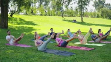 Yoga grubu güneşli parkta tekne pozu veriyor. Çekirdek kuvvetiyle dengeli çalışma için doğanın sükunetini birleştiriyorlar. Sağlıklı yaşam tarzını kabul et