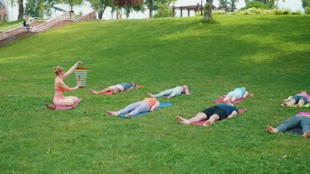 女性在集体冥想时敲响警钟 参与者在公园练习瑜伽后在垫子上放松 并与自然环境中的愈合色调相协调 — 图库视频影像