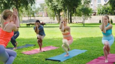 Yoga sınıfı, yetenekli bir eğitmenin desteklediği denge ve konsantrasyon gösterisi olan güneşli bir parkta Kartal Pozu sergiliyor.