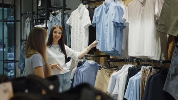 Duas Mulheres Examinam Prateleiras Roupas Loja Uma Selecionando Camisa Azul — Vídeo de Stock