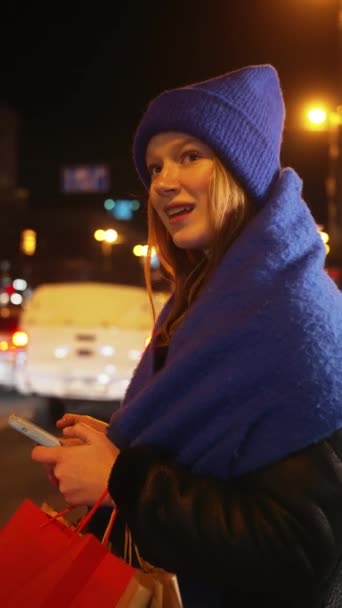 Eine Lächelnde Frau Mit Blauem Hut Und Einkaufstaschen Telefoniert Nachts — Stockvideo