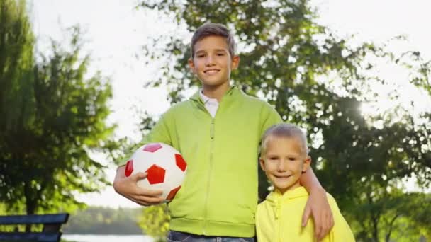 兄弟俩站在一起 拿着足球 对着镜头笑着 培养出一种友谊和体育精神 兄弟情谊和运动精神 — 图库视频影像
