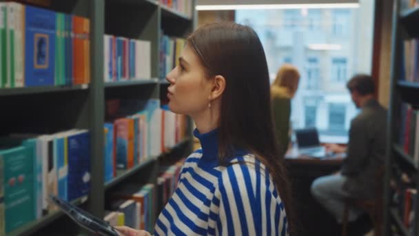 Mavi Beyaz Çizgili Süveter Giyen Genç Bir Kadın Kütüphane Rafından — Stok video