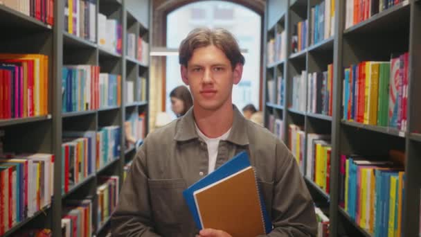 以男生为重点的学生站在图书馆架子之间 手持笔记本 准备学习或研究 — 图库视频影像