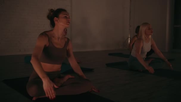 妇女们在安静的瑜伽演播室里表演伸展姿势 在柔和的夜光的照耀下 在和平的集体对话中专注于平衡和灵活性 健康与团体健身概念 — 图库视频影像