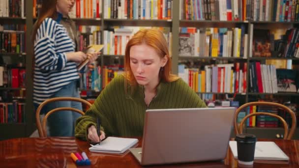 Odaklanmış Yeşil Kazaklı Öğrenci Laptopuyla Çalışıyor Renkli Kütüphanedeki Masada Notlar — Stok video