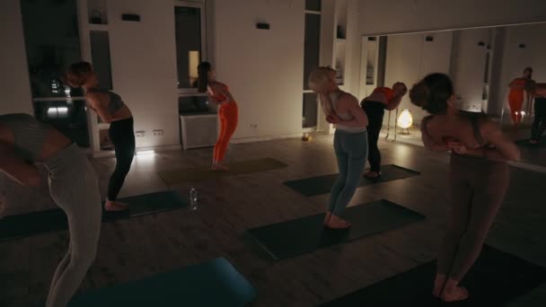 瑜伽课上的女生在灯光昏暗的房间里做伸展运动 一组人在晚上的演播室里表演背弯姿势 用柔和的灯光照明 反射镜反映他们的姿势 — 图库视频影像