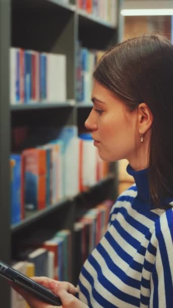 Layar Vertikal Wanita Muda Berbaju Biru Dan Putih Memilih Buku — Stok Video