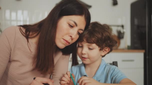 母亲专心地帮助她年幼的儿子在家里做着创造性的工作 在家庭团聚的时刻 在家专心养育子女的温馨时刻 — 图库视频影像