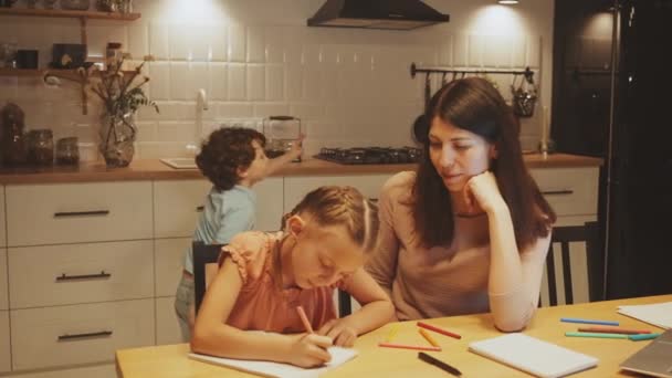 Madre Supervisa Hija Dibujando Mesa Cocina Mientras Hijo Distrae Juguetonamente — Vídeo de stock