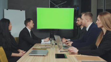 İş dünyasından profesyonellerden oluşan bir ekip yeşil ekran monitöründen sunumu dikkatle izliyor, yüksek teknolojili toplantı odasında etkileşime geçmeye hazır. Video konferans çağrısına yöneticiler katılıyor