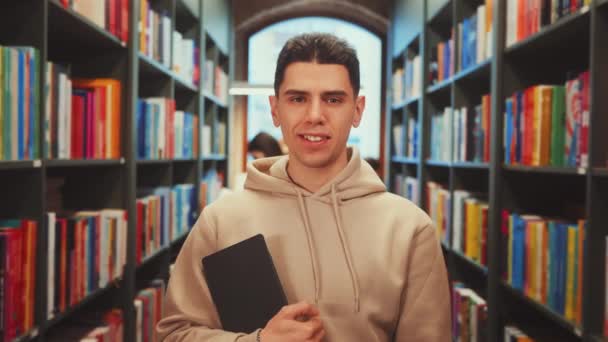 Young Man Stands Confidently Library Aisle Holding Book Smiling Camera — Stock Video