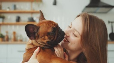 Neşeli kadın, Fransız Bulldog 'u parlak mutfakta yüzünü yalarken yürekten gülüyor. Sevgi ve mutluluk dolu evcil hayvan ve sahibi arasında özel bir bağ vardır.