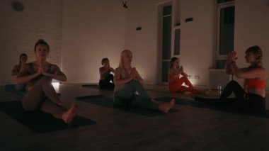 Yoga stüdyosunun loş ışıklarındaki bireyler Anjali Mudra ile yan yana oturdular. Poz, omurga dönüşüyle özenli solunumu birleştirerek esneklik ve iç sakinliği arttırır.