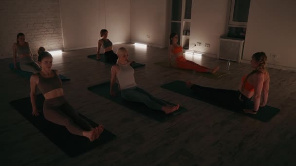 一组人正在练习瑜伽 专注于他们的核心和平衡 当他们做反平面姿势的时候 光线昏暗的房间为晚上的锻炼营造了一种宁静的气氛 — 图库视频影像